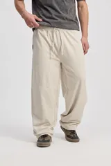 Pantalón de algodón color beige, de corte holgado y pierna amplia, con cintura elastizada y cordón ajustable.
