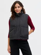 Chaleco acolchado color negro con diseño matelaseado de ondas, cuello alto, cierre frontal con cremallera y bolsillos frontales aplicados.
