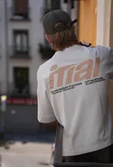 Remera color crema de corte holgado con mangas cortas y estampado en la espalda con el logo de la marca Ittai en color marrón.