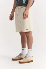 Bermuda de algodón sin frisa, color beige, con textura marcada, cintura elastizada con cordón ajustable, bolsillos laterales y detalle de logo bordado.