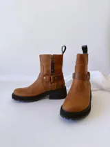 Bota de cuero color marrón con suela de goma negra, cierre lateral y pulsera desmontable con hebilla.