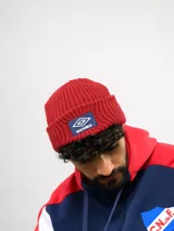 Gorro tipo beanie tejido en color rojo, con diseño acanalado y parche frontal con el logo de Umbro y la inscripción Nacional.