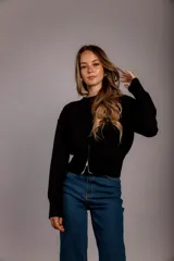 Suéter de punto color crema, con cuello redondo, manga larga y cierre frontal parcial que deja ver parte del abdomen.