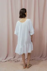 Vestido corto blanco de lino, con diseño suelto y holgado, mangas amplias hasta los codos, escote redondo con abertura en V y lazo decorativo, y un volante en la parte inferior.