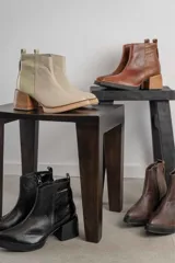 Bota corta de cuero negro con acabado combinado mate y charol. Presenta una tira decorativa con tachas metálicas y hebilla en el tobillo, tacón cuadrado robusto y suela con plataforma.