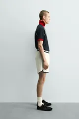 Polo de corte relajado confeccionado en tejido de algodón con estructura abierta. Presenta cuello polo con abertura frontal en V, mangas cortas tipo ranglán y acabados en rib a contraste en color rojo y blanco.