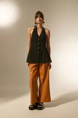 Chaleco largo negro, con escote halter y abertura frontal con botones joya. Corte entallado en la parte superior y ligeramente acampanado en el bajo.