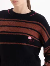 Sweater de punto a rayas horizontales en color negro y marrón, con cuello redondo y detalles de costuras en color fucsia. Presenta un pequeño bordado de un flamenco en el pecho y un detalle bordado en el puño.