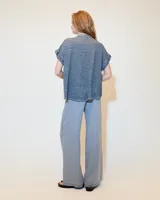 Remera blanca de lino con cuello mao, media cartera con broches metálicos y manga japonesa. Presenta un bolsillo frontal tipo plaqué, recortes laterales en sisa con detalles de encaje y ruedo redondeado con corte escalonado.