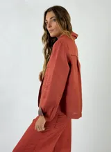 Chaqueta de lino color tostado, con diseño de corte recto, cuello camisero, cierre frontal con botones y bolsillos frontales con solapa. Presenta detalles en color crudo en el interior del cuello y los puños.