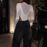 Body de manga larga confeccionado en tela semitransparente color blanco, con diseño de paneles estructurados y cuello alto.
