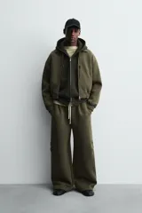 Pantalón de corte wide fit confeccionado en tejido técnico compacto con efecto neopreno. Presenta cintura elástica con cordón ajustable, pliegues frontales, bolsillos laterales y detalle de pliegues en las rodillas con aplicaciones metálicas.