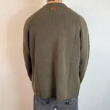 Sweater verde oliva de tejido grueso con cuello alto y mangas raglán. Corte holgado.