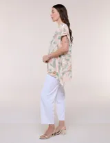 Blusa de silueta holgada confeccionada en crepé liviano, con estampado abstracto en tonos rosados, verdes y blancos. Presenta escote redondo amplio, hombros caídos con hilera de botones decorativos, mangas cortas con dobladillo y ruedo asimétrico en picos.
