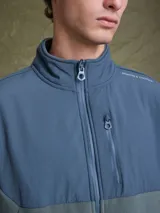 Campera de polar con cierre frontal completo, cuello alto y bolsillo en el pecho con cierre. Presenta un diseño combinado con paneles de tela técnica en la parte superior y polar en el resto de la prenda, con logo de la marca Benson & Thomas estampado en el hombro.