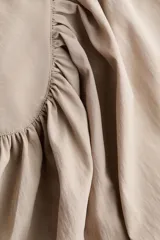 Blusa capa color beige con cuello alto, hombreras y diseño acampanado con frunces.