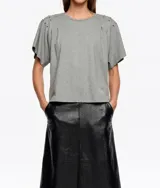 Camiseta de corte recto y escote redondo, con mangas cortas que presentan pliegues en los hombros y detalle de remaches metálicos decorativos.