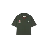 Remera polo de manga corta de Eme Studios, color verde militar, con cuello en V y detalles en rojo y blanco. Cuenta con un parche bordado estilo escudo con la palabra "GOLF" en el pecho derecho y la inscripción "EMESTUDIOS GOLF" bordada en el izquierdo.