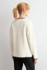 Sweater de punto color crudo con escote en V, manga larga y detalles de bordado en color negro en el escote y los puños.