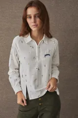 Remera estilo polo de manga larga, confeccionada en una mezcla de algodón y lino. Presenta un cierre frontal parcial, cuello camisero y aberturas laterales en el frente. El diseño incluye un estampado integral con motivos deportivos y un detalle bordado en el pecho.