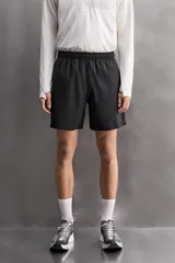 Pantalones cortos deportivos color marrón rojizo, confeccionados en tejido técnico ligero y elástico. Presentan cintura elástica ajustable con cordón interior, bolsillos frontales y un bolsillo trasero con cierre de cremallera. Los laterales tienen perforaciones para transpirabilidad y aberturas laterales en el bajo.