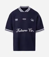 Remera de tejido texturizado color azul marino, con cuello redondo y mangas cortas con puños a rayas blancas. Presenta bordados frontales con la inscripción 'Future Co.', el número '98', un logo ovalado y estrellas.