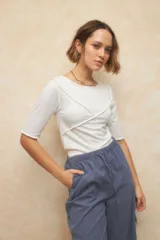 Remera blanca de punto con mangas tres cuartos, escote redondo y detalle de costuras superpuestas de forma asimétrica.