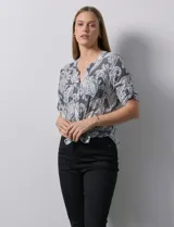 Blusa celeste con estampado blanco, de gasa, con cuello a la base y escote en V. Tiene abertura con botones, bolsillos delanteros y mangas 3/4 regulables con presilla y botón. El ruedo termina con un nudo.