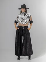 Pantalón tipo palazzo de corte oversized, confeccionado en tela con textura aterciopelada en color negro. Presenta cintura alta con pinzas, bolsillos laterales y un cinturón ancho integrado con hebilla al tono.