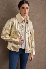 Campera de cuero metalizado color dorado con cuello de corderito sintético en tono crema. Presenta cierre frontal con botones metálicos, bolsillos frontales con solapa y diseño de corte recto.