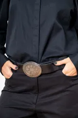 Cinturón de cuero negro con textura rugosa y hebilla ovalada de metal envejecido con diseño de puntos en relieve.
