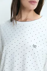 Pijama de dos piezas compuesto por remera de manga larga y pantalón, confeccionado en algodón blanco con estampado de lunares negros. La remera presenta cuello redondo y un pequeño bordado de corazones en el pecho.