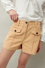 Short de algodón de tiro alto, color beige, con bolsillos delanteros tipo parche con solapa y botones a la vista.