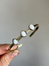 Pulsera rígida de bronce color dorado con tres piedras de ágata blancas de forma ovalada.