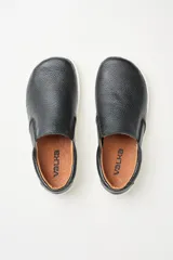Championes slip-on negros de cuero graneado, con elásticos laterales para un calce rápido. Tienen plantilla forrada en cuero y suela fina, flexible y plana (zero drop).