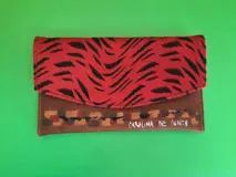 Sobre de mano Carolina De Cunto modelo Murcia, confeccionado en cuero marrón con solapa de pelo animal print en tonos rojo y negro, con detalles pintados a mano en la parte inferior.