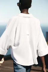 Camisa blanca de lino con cuello solapa, escote pico, manga ancha por debajo del codo con vuelta y bajo asimétrico.