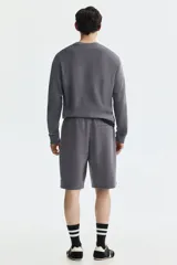 Short de felpa interlock color gris oscuro, con cintura elástica fruncida y cordón ajustable. Presenta un diseño de corte relajado a la rodilla, bolsillos laterales y bolsillos traseros.