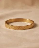 Pulsera tipo esclava rígida de acero con baño de oro, con diseño geométrico grabado en toda su superficie.