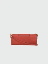 Cartera tipo crossbody de cuero color terracota, con forma cilíndrica, solapa frontal con cierre de botón a presión metálico y correa ajustable. Incluye un colgante decorativo de cuentas coloridas en uno de los laterales.