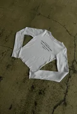 Remera blanca de manga larga con estampa tipográfica en el pecho y terminaciones con dobladillo ondulado.