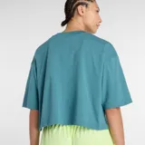 Remera de corte cropped y diseño oversize, color verde azulado, con cuello redondo y mangas cortas. Presenta un estampado frontal con el logo de la marca en colores amarillo neón y rosa.