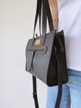 Cartera tipo tote bag de cuero color negro, con doble asa corta de mano y correa larga regulable y extraíble para usar al hombro o cruzada. Tiene un bolsillo frontal con cierre y un bolsillo interno.