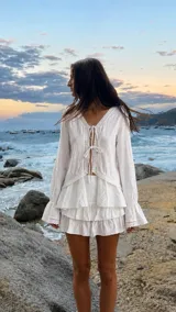 Blusa blanca de manga larga con escote en V y cierre frontal con cordones para atar. Presenta detalles de encaje en los bordes y terminación acampanada en las mangas.