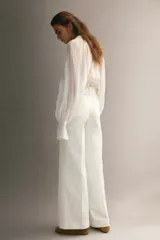Jean de denim de algodón blanco con leve elasticidad, tiro alto y diseño de pierna ancha (wide leg). Cuenta con bolsillos de parche delanteros, botón metálico con diseño y pliegues marcados al frente y en la espalda.