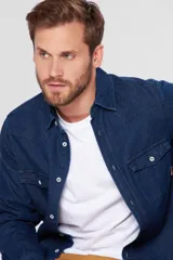 Camisa de jean azul con mangas largas, bolsillos en el pecho, corte en los hombros y detalle en la espalda. Tiene botones personalizados y detalles en cuero.