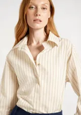 Camisa de manga larga con cuello clásico y cierre frontal con botones. Presenta un diseño a rayas verticales en tonos beige y crema.