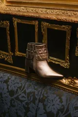 Botas cortas de cuero negro con taco cuadrado y punta fina. Presentan cuello caído capitoneado con apliques brillantes y cierre lateral con cremallera.