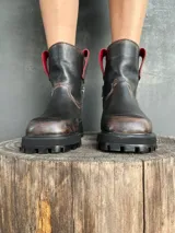 Bota de cuero con efecto desgastado en tonos marrones y negros, con suela track robusta y cierre lateral. Presenta detalles en color rojo en la parte superior de la caña.