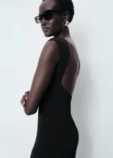 Vestido midi de corte recto y diseño minimalista, confeccionado en tejido elástico. Presenta cuello barco, tirantes anchos, espalda abierta y una abertura posterior en el bajo.